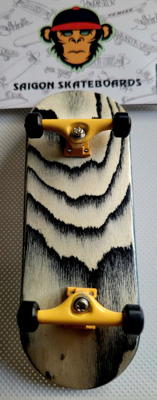 Saigon Skateboards fingerboard with black-and-cream streaked deck and yellow trucks