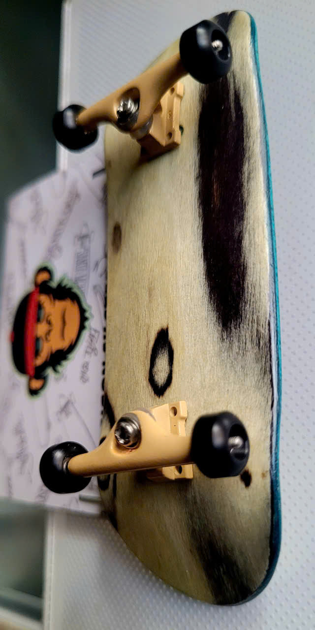 Fingerboard underside showing natural wood grain, beige trucks, and black wheels