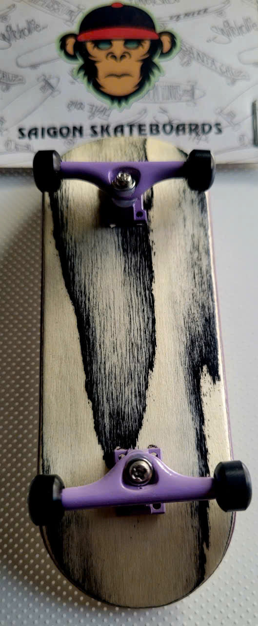 Fingerboard with black streaks across a pale wood deck, purple trucks, and black wheels